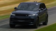 a black range rover driving on a road with grass and trees in the back ground