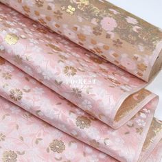 three rolls of pink and gold brocaded fabric with flowers on the side,