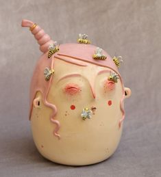 a ceramic head with bees on it's ears and nose, against a gray background