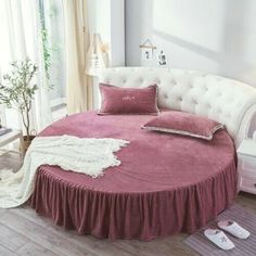 a round bed with pink bedspread and pillows on it in a white room