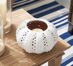 a white candle holder sitting on top of a wooden table next to a glass vase