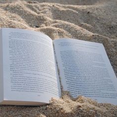 an open book sitting on top of a sandy beach