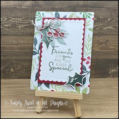 a christmas card with holly and berries on it, sitting on a wooden easel