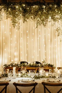 the table is set for dinner with candles and greenery hanging from the wall behind it