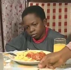 a young boy sitting at a table with a plate of food in front of him