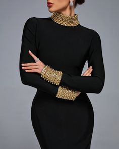 a woman with her arms crossed wearing a black dress and gold bracelets on her arm