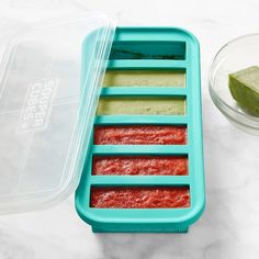 an ice tray with four different colored popsicles and a lime slice on the side