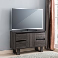 a flat screen tv sitting on top of a wooden cabinet in front of a window