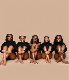 five women in black bodysuits sitting on the ground with their legs crossed and smiling