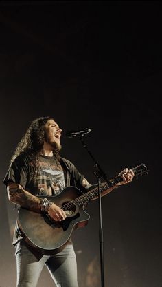 a man singing into a microphone while holding a guitar in front of him on stage