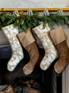 three stockings hanging from a mantel with pine cones on top and evergreen branches in the background