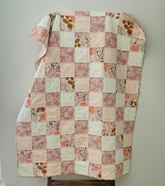 a pink and white patchwork quilt hanging on a wall next to a wooden chair