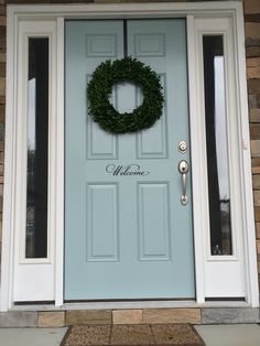 a blue front door with a wreath on it and welcome written on the side panel