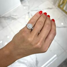 a woman's hand holding a diamond ring on her left hand with red nails