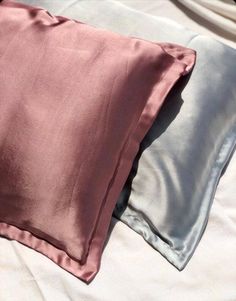 two pillows sitting on top of a bed with white sheets and pink pillowcases