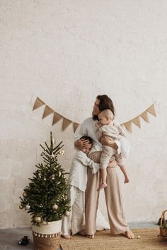 a woman holding a baby in her arms next to a small christmas tree and garland