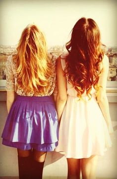 two girls looking out over the city with their backs to each other, one is holding her hand