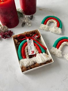 two christmas wreaths in a gift box with red candles and pine cones on the side