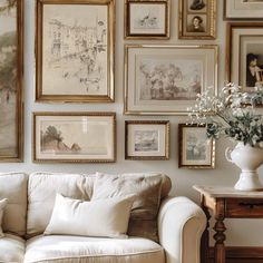 a white couch sitting in front of a wall covered with pictures and vase filled with flowers