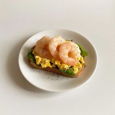 a white plate topped with a sandwich filled with eggs and shrimp on top of lettuce