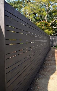 the side of a black fence with wooden slats on it and trees in the background