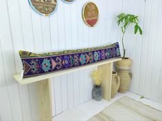 a bench with a colorful cushion on it in front of some vases and plants