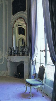 a chair sitting in front of a window next to a fire place and a mirror