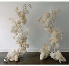 two tall white vases with flowers in them sitting on the floor next to each other