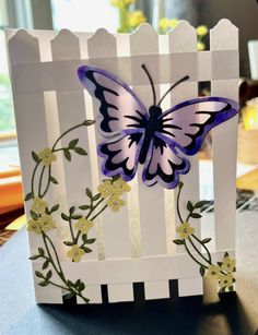 a card made to look like a butterfly on a white picket fence with yellow flowers