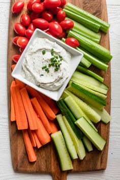 a wooden cutting board topped with cucumbers, carrots and celery