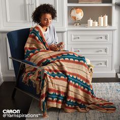 a woman sitting in a chair with a blanket on her lap looking at her cell phone