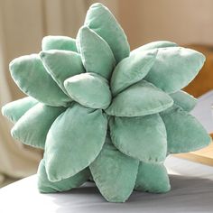 a green stuffed plant sitting on top of a bed next to a cup and saucer