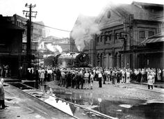 an old black and white photo of people standing in front of a train on the tracks