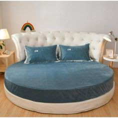 a large round bed with blue pillows on top of it and a rainbow in the background