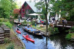 several canoes are parked on the side of a river as people stand near by