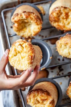 a person holding up a muffin in front of other muffins on a baking tray