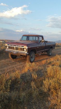 an old pick up truck parked on the side of a dirt road near dry grass