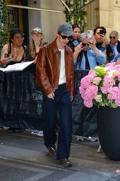 a man is walking down the street in front of a large flower pot with pink flowers