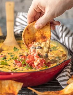 a person dipping tortilla chips into a red skillet filled with quesadilla soup