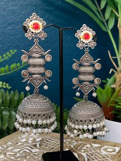 This silver replica statement jhumki earring is crafted with exquisite detail and superior quality. With a combination of kemp stone, kundan work, and pearl drop, these lightweight earrings are sure to be a stylish statement piece. About 4.5inch long and 1.5 inch wide Silver Meenakari Chandbali Pearl Earrings, Traditional Silver Kundan Pearl Earrings, Silver Kundan Bollywood Jhumkas, Silver Meenakari Drop Pearl Earrings, Silver Meenakari Pearl Earrings For Festive Occasions, Silver Temple Jewelry Danglers With Stone Work, Metal Chandbali Danglers With Meenakari, Silver Meenakari Kundan Chandelier Earrings, Silver Kundan Chandelier Earrings With Meenakari