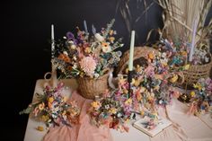 a table topped with flowers and candles next to a basket filled with fake flowers on top of a cloth covered table