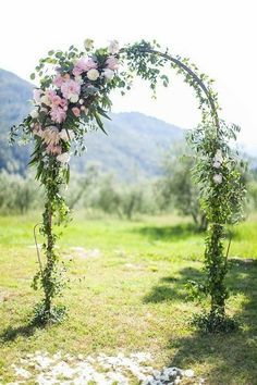 an outdoor wedding arch with pink flowers and greenery on the ground in front of mountains