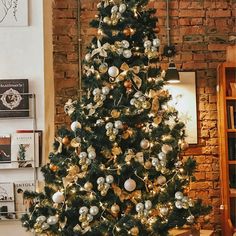 a decorated christmas tree with gold and silver ornaments in a living room next to a brick wall