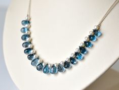 This sumptuous necklace would be the perfect "something blue" for a bride-to-be! The fine-cut facets of the midnight blue teardrops contrast beautifully with the lustrous white pearls. The elegant curve of the necklace would work well with a sweetheart, strapless, or scooped neckline.   Micro-faceted London Blue Topaz teardrops are combined with white freshwater pearls and fine sterling silver chain. Necklace is finished with a sterling silver spring clasp and a 2.5" adjustable chain. Necklace m Blue Gemstone Wedding Necklace, Blue Briolette Necklace For Anniversary, Blue Briolette Necklace For Wedding, Wedding Blue Topaz Faceted Jewelry, Blue Briolette Pearl Necklace For Gift, Sapphire Faceted Jewelry For Wedding, Sapphire Gemstone Necklace For Wedding, Blue Topaz Necklace For Wedding, Blue Gemstone Beads Necklace For Wedding