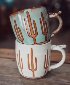 two cups with cactus designs on them sitting side by side, one is blue and the other has brown