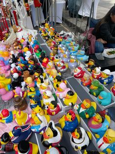 several rows of rubber ducks on display at an outdoor market with people sitting around them