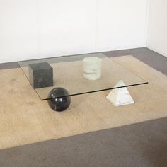 a glass table sitting on top of a floor next to a black ball and vase