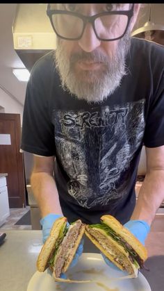 a man with glasses and a beard holding a sandwich on a plate in front of him