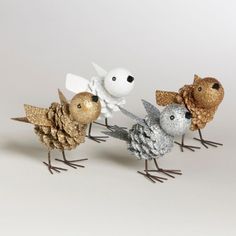 three metal birds are standing next to each other on a white surface with pine cones