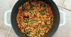 a pot filled with pasta and spinach on top of a tile floor next to a wooden spoon